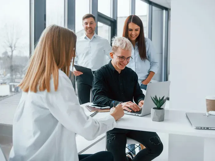 Group of young professionals having a discussion around a laptop in a bright modern office workspace